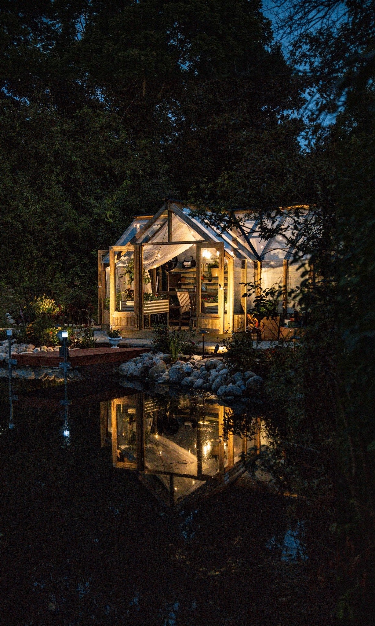A lit Nordwood greenhouse reflected in the pond at night
